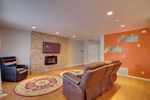 A living room with a stone wall, a flat-screen TV, a leather recliner, a patterned rug, and a wooden floor. - Extended Stay w/ Hot Tub! 5 Mi to Old Town ABQ (Albuquerque)