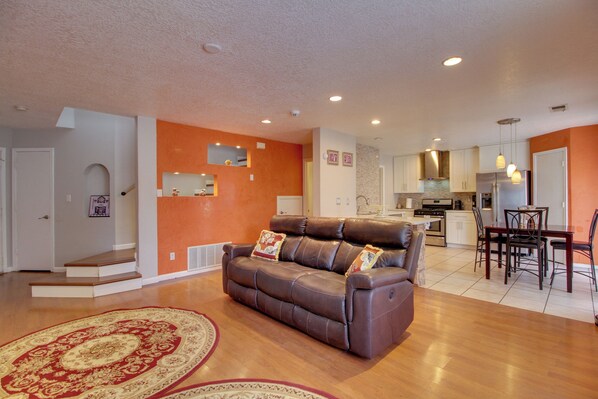 A living room with a brown leather sofa, a dining table with chairs, a kitchen area, and a staircase leading to another level. - Extended Stay w/ Hot Tub! 5 Mi to Old Town ABQ (Albuquerque)