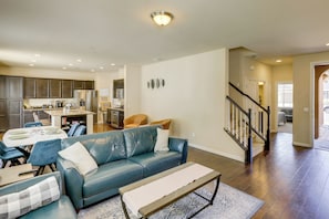 A modern living room with a blue leather sofa, a dining table, and a kitchen in the background.