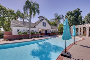 Une piscine avec un bâtiment en arrière-plan, entourée de palmiers et d’un patio couvert.
