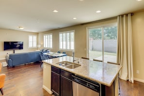 A modern kitchen with a built-in dishwasher, a dining area with a table and chairs, and a living room with a sofa and TV.