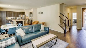 A modern living room with a blue leather sofa, a dining table, and a kitchen in the background. - Fenced Yard! Family Escape, 1 Mi to Csub (Bakersfield)
