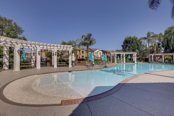 Une piscine agrémentée d’une pergola, de chaises longues et de parasols.