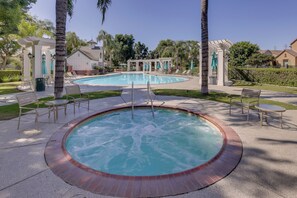 A pool area with a hot tub, lounge chairs, and a pergola.