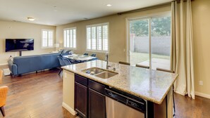 A modern kitchen with a built-in dishwasher, a dining area with a table and chairs, and a living room with a sofa and TV. - Fenced Yard! Family Escape, 1 Mi to Csub (Bakersfield)