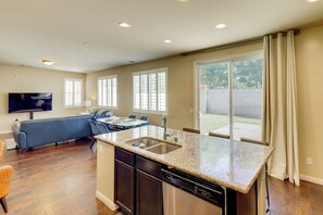 A modern kitchen with a built-in dishwasher, a dining area with a table and chairs, and a living room with a sofa and TV. - Fenced Yard! Family Escape, 1 Mi to Csub (Bakersfield)