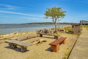 A beachside picnic area with benches and a tree, overlooking a body of water and a distant mountain. - Beachfront Oasis! Luxe Lummi Island Retreat (Lummi Island)