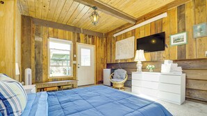 A bedroom with a large bed, wooden walls, a television, and a window. - Beachfront Oasis! Lummi Island Family Getaway (Lummi Island)