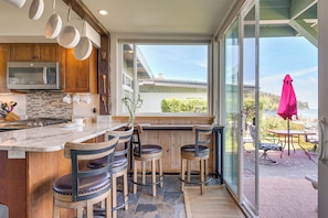 A kitchen with a large island, wooden chairs, and a view of the outdoors. - Beachfront Oasis! Luxe Lummi Island Retreat (Lummi Island)