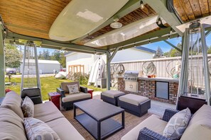 Un patio al aire libre con mobiliario de mimbre, una parrilla y una zona cubierta con techo de madera.