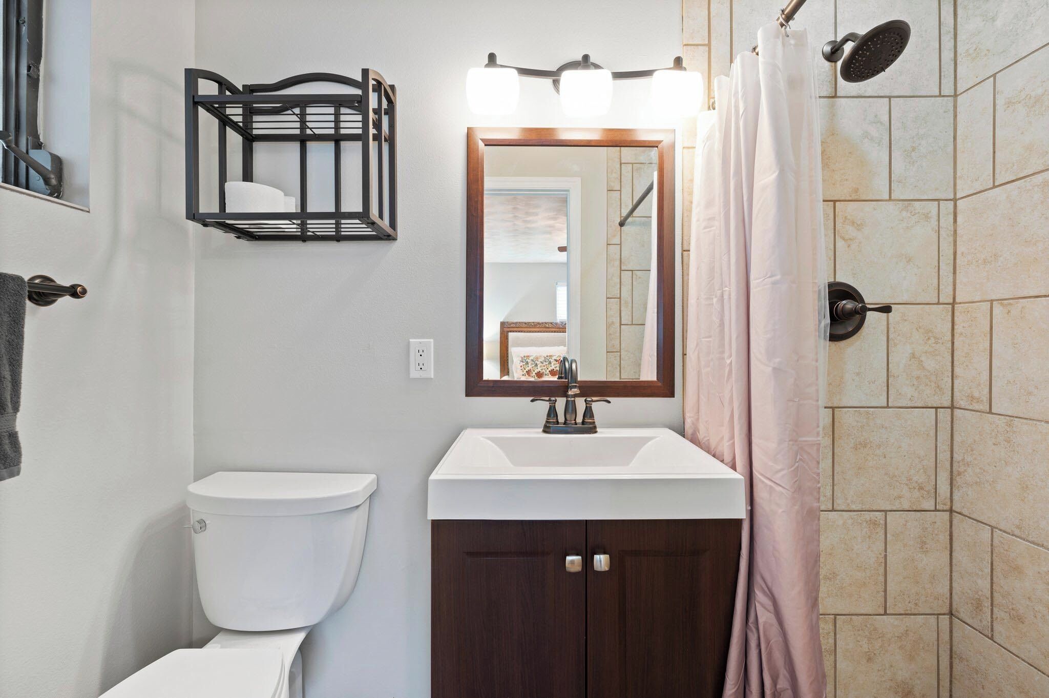 A bathroom with a toilet, sink, mirror, shower, and a towel rack.
