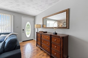 Quarto com penteadeira de madeira, espelho, luminária e janela com persianas.