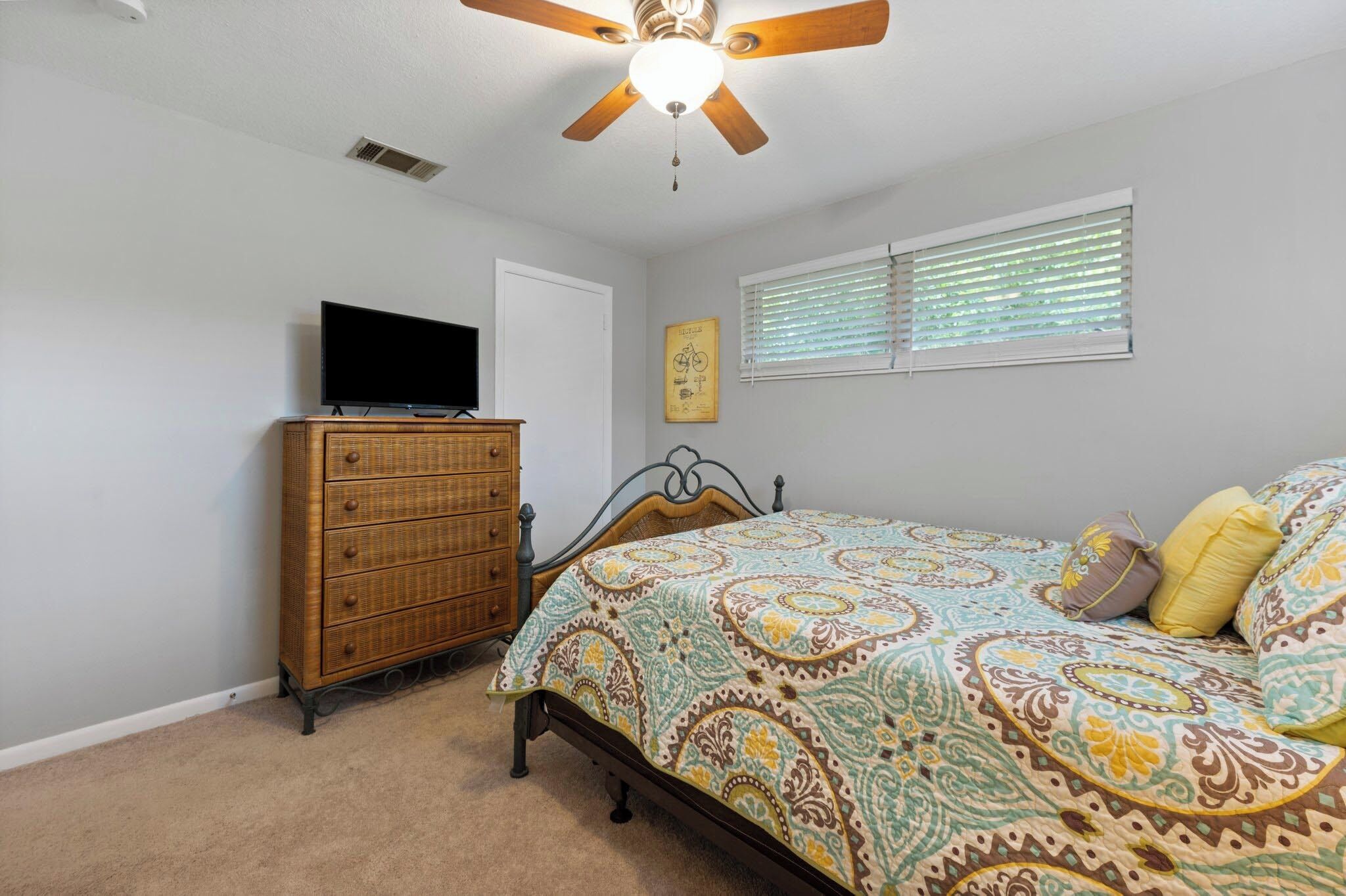 A bedroom with a bed, a dresser, a television, a ceiling fan, and a window with blinds.