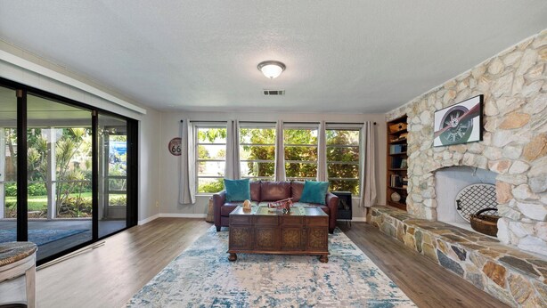 A living room with a stone fireplace, a leather sofa, and a large window. - 15 Min to Beaches! Fenced Yard, Screened Lanai (Melbourne)