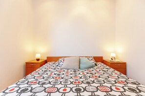 A bed with a patterned bedspread, two bedside lamps, and wooden nightstands. - Apartment Mondo A2 (Dubrovnik)