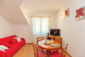 A room with a red sofa, a wooden dining table with chairs, a television, and artwork on the wall. - Apartment Mondo A2 (Dubrovnik)