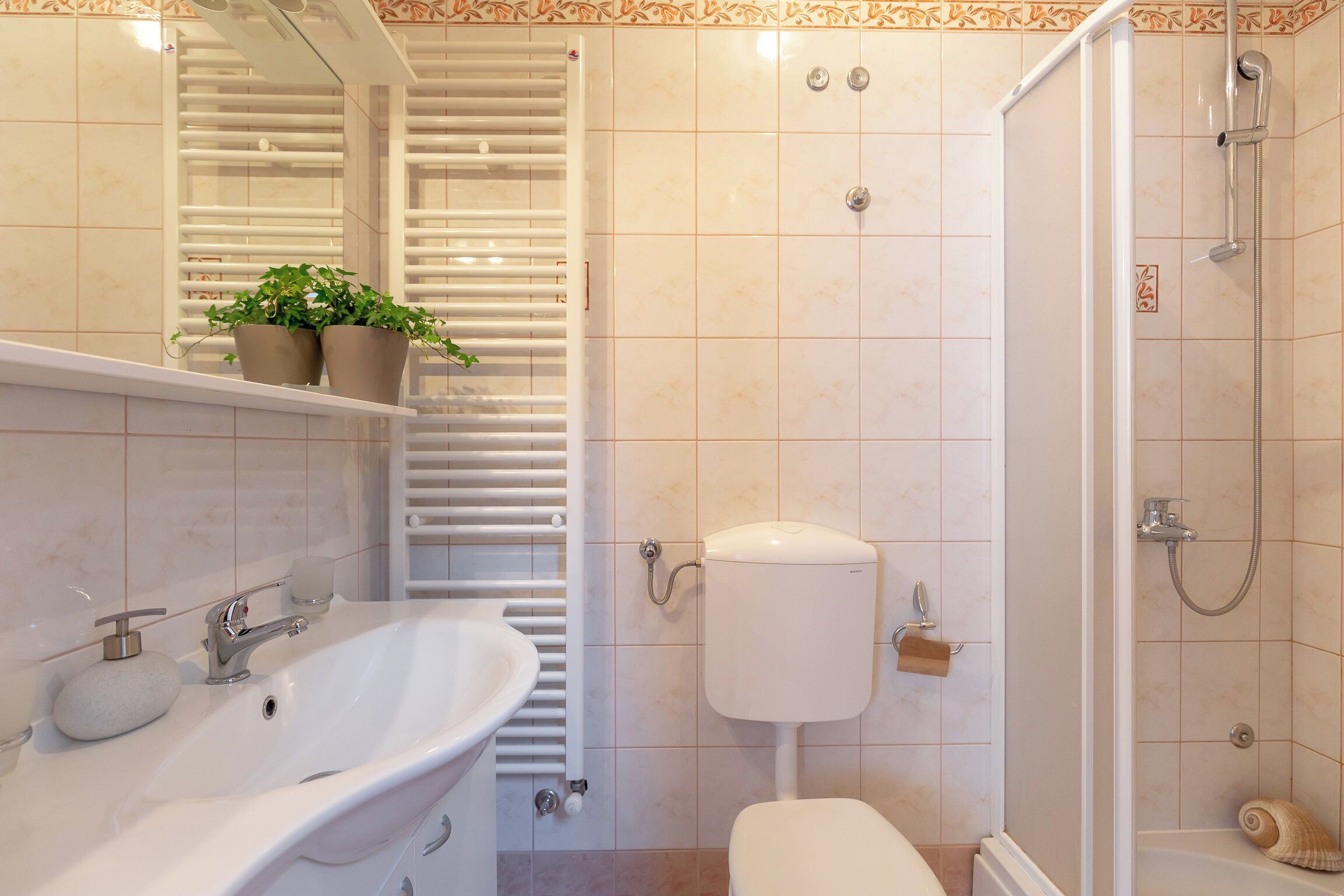 A bathroom with a sink, toilet, shower, and a towel rack with plants.