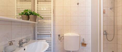 A bathroom with a sink, toilet, shower, and a towel rack with plants.