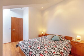 A bedroom with a bed, bedside tables, a wooden door, and a light fixture. - Apartment Mondo A2 (Dubrovnik)