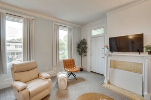 Ein Wohnzimmer mit einem beigen Ledersofa, einem kleinen runden Hocker, einer Topfpflanze, einem Kamin und einem Fernseher.