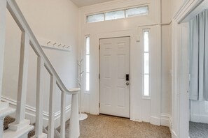 Ein heller Innenbereich mit einem Flur, einer geschlossenen Tür, einer Treppe mit weißen Geländern und einem Teppichboden.