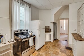 Eine Küche mit Herd, Backofen, Mikrowelle, Kühlschrank und einem Fenster mit Vorhängen.