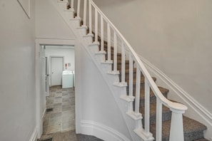 A staircase with white balusters and a carpeted floor leading to a room with a white door and a white appliance.