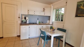 A compact kitchen with white cabinets, a small refrigerator, a coffee maker, and a dining table with chairs. - Le Paille en Queue : Studio with sea view and saltwater swimming pool, quiet garden with trees (Saint-Leu)