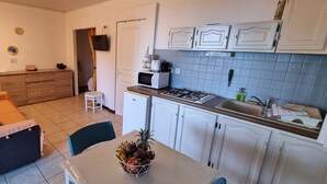 A compact living space with a kitchenette, a dining area, and a sofa. - Le Paille en Queue : Studio with sea view and saltwater swimming pool, quiet garden with trees (Saint-Leu)
