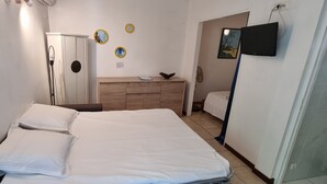 A room with a bed, a wooden dresser, a mirror, and a television on the wall. - Le Paille en Queue : Studio with sea view and saltwater swimming pool, quiet garden with trees (Saint-Leu)