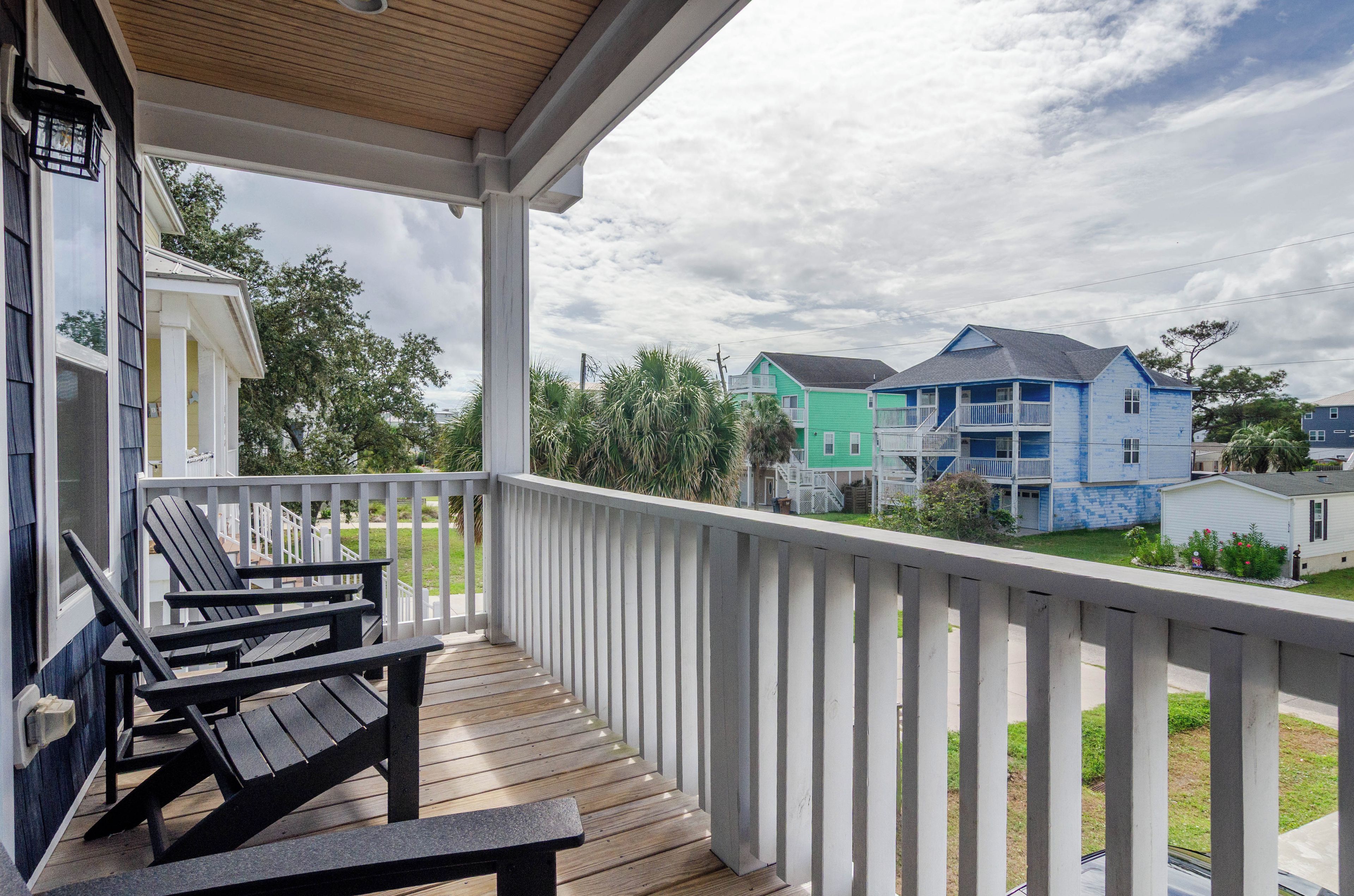 A wooden deck with a white railing, a bench, and a view of colorful houses in the background.