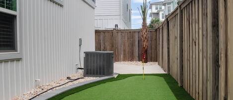 A backyard with artificial grass, a golf hole, and a flagstick.
