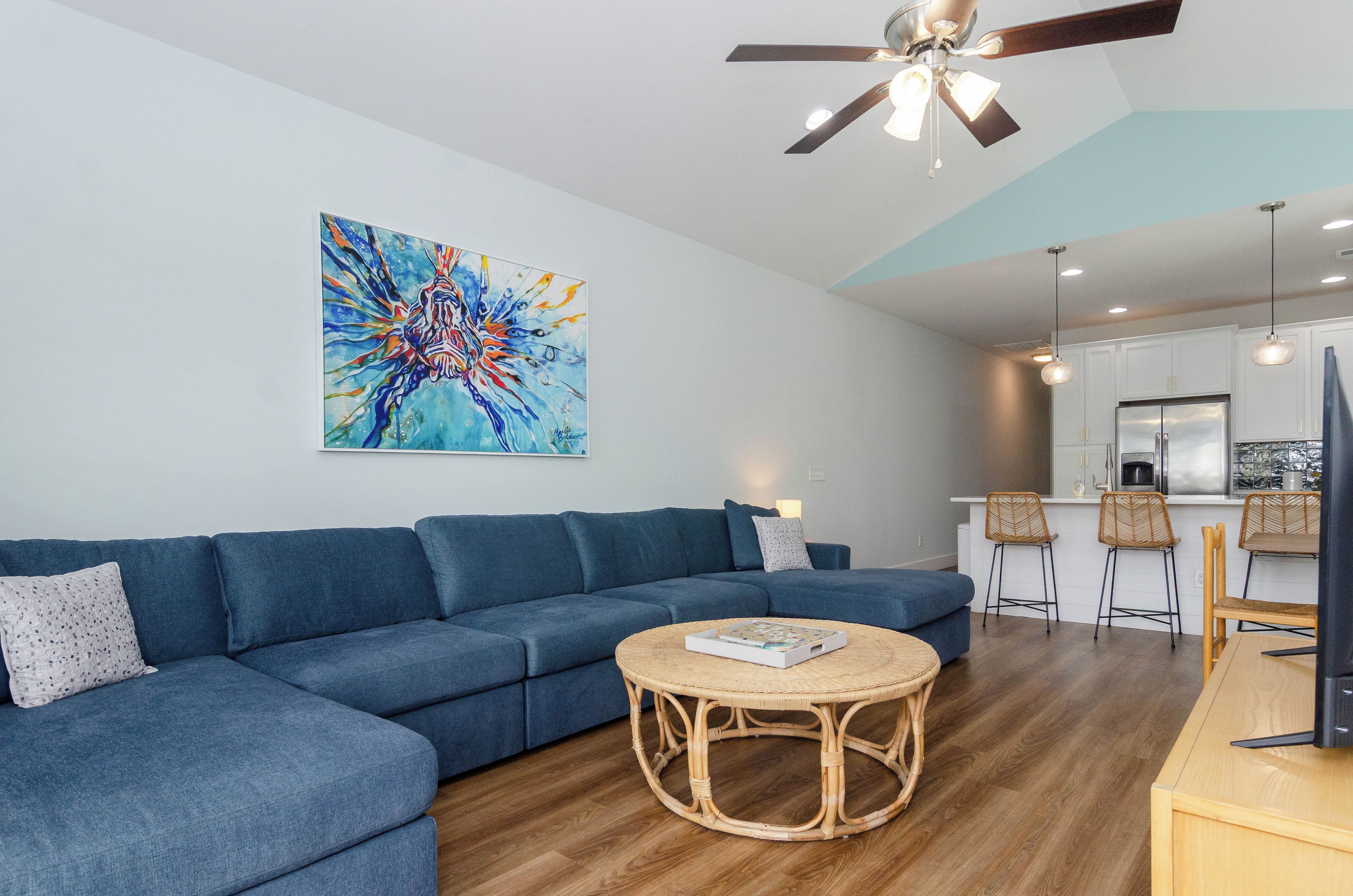 A modern living room with a blue sofa, a round wicker coffee table, and a ceiling fan.