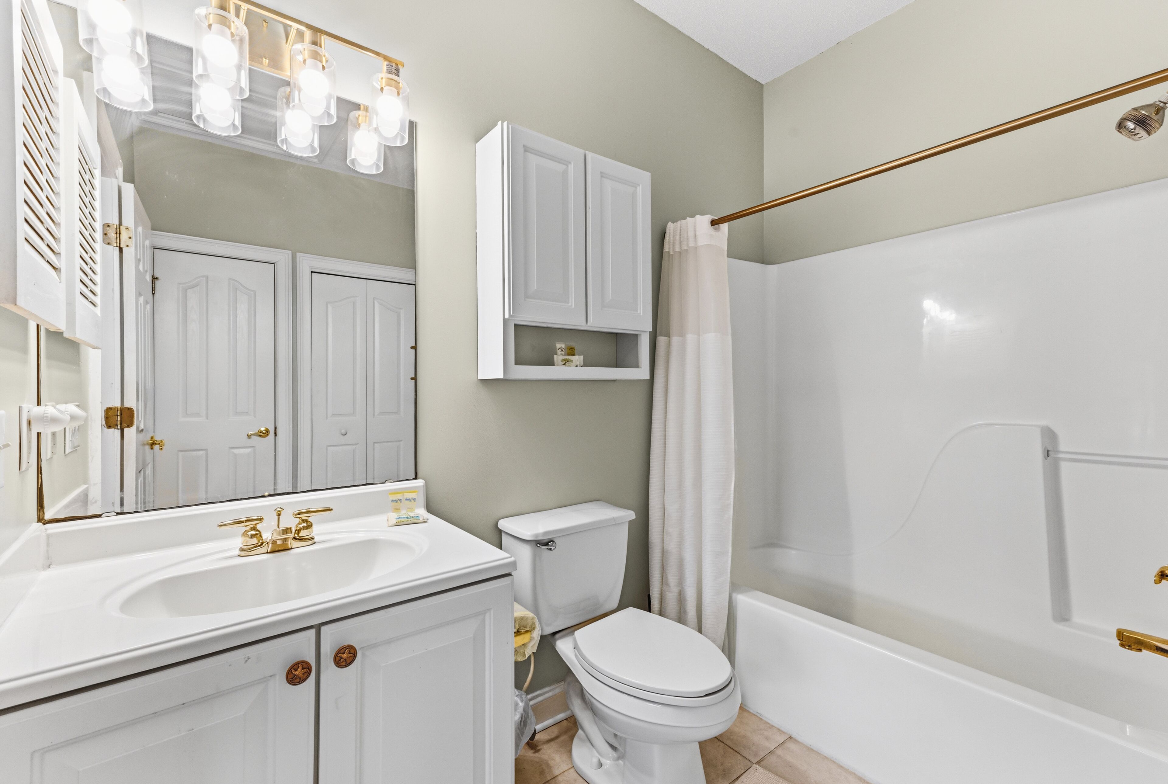 A bathroom with a white sink, toilet, and bathtub. There are white cabinets above the toilet and a mirror above the sink.