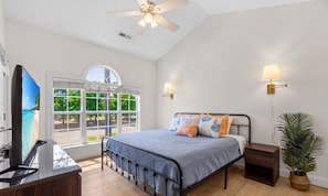 Ein Schlafzimmer mit Bett, Fernseher, Deckenventilator, Fenster und einer Wandlampe.