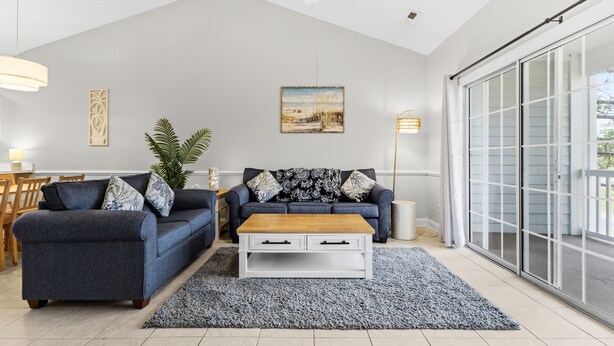 Een woonkamer met een grijze bank, een houten salontafel en een groot raam met uitzicht.