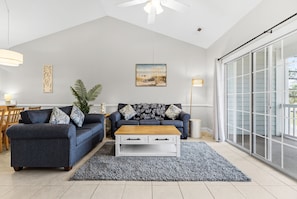 Ein Wohnzimmer mit grauem Sofa, einem Holztisch und einem großen Fenster mit Blick.