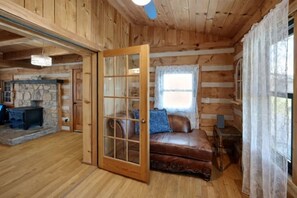 Een blokhutinterieur met een stenen openhaard, een leren bank en een houten deur.