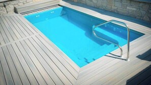 Una piscina con una escalera metálica, rodeada de una terraza de madera.
