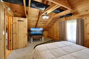Een houten kamer met een bed, een televisie en een raam.