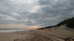 En strand med en sandsti, der fører ud til havet, under en overskyet himmel.