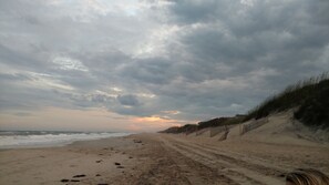 Une plage avec un sentier sablonneux menant à la mer, sous un ciel nuageux.