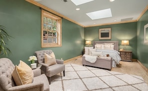 A bedroom with a bed, two bedside tables, a chair, a window, and a ceiling skylight. - Hunts Point | Waterfront Estate & Guest Villa (Hunts Point)