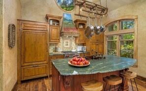 A kitchen with wooden cabinets, a marble island, a stove, and a window with a view of greenery. - Hunts Point | Waterfront Estate & Guest Villa (Hunts Point)
