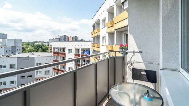 Un balcón con una mesa de vidrio, una silla y vistas a edificios cercanos.