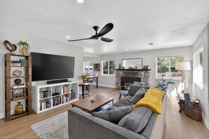 A modern living room with a flat-screen TV, a ceiling fan, a fireplace, and a dining area. - Historic Placerville 3BR Sleeps 6 AppleHill (Placerville)