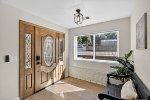 A wooden door with glass panels, a bench with a cushion, a window with a view of a parking area, and a wall-mounted light fixture. - Historic Placerville 3BR Sleeps 6 AppleHill (Placerville)