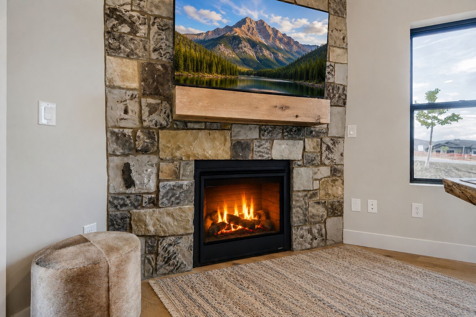 A stone fireplace with a TV above it, a cozy chair, and a view of mountains through a window.