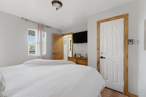 Un dormitorio con una cama grande, una puerta de madera, un televisor y una ventana con cortinas.
