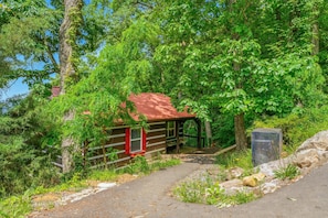 A rustic cabin with a red roof, surrounded by dense greenery and a dirt path leading to it. - Red Maple 3 Bedroom Cabin (Sevierville)